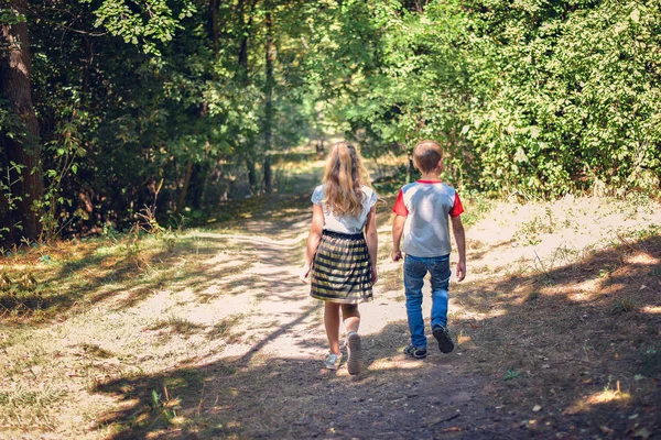 Um menino e uma menina caminham ao longo de um caminho na floresta — Fotografia de Stock