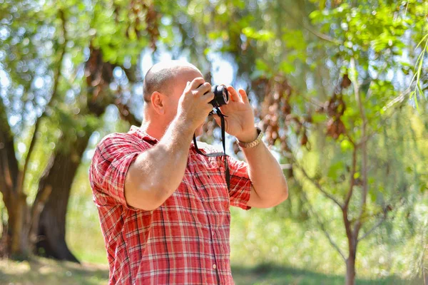 Mężczyzna fotograf trzyma kamerę w pobliżu jego twarzy i robienia zdjęć na aparacie w parku. — Zdjęcie stockowe