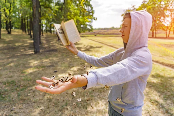 Un uomo legge un libro nel parco, lettere volano dall'alto e cadono sulla sua mano, conoscenza esaustiva della natura . — Foto Stock