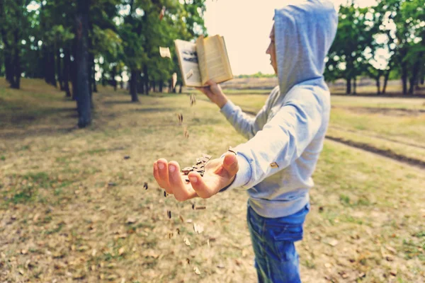 Człowiek czyta książkę w parku, listów latać z góry i spadnie na rękę, wyczerpująca wiedza w przyrodzie. — Zdjęcie stockowe