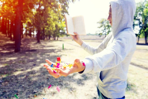 Un hombre lee un libro en el parque, las cartas vuelan desde arriba y caen sobre su mano, el conocimiento exhaustivo en la naturaleza . —  Fotos de Stock