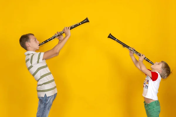 Due ragazzi suonano il clarinetto e lo reggono su uno sfondo giallo . — Foto Stock