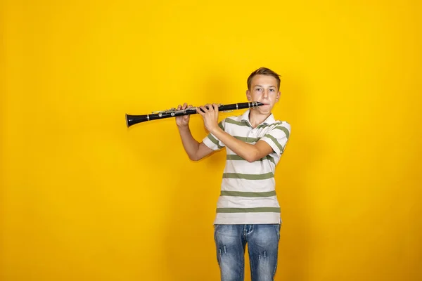 Boy musician playing the clarinet on a yellow background. — Stock Photo, Image