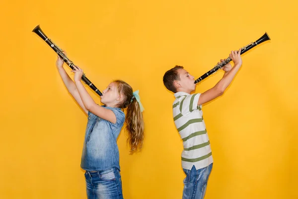Un ragazzo e una ragazza con i clarinetti stanno in piedi con le spalle l'uno all'altro, suonando il clarinetto, su uno sfondo giallo . — Foto Stock