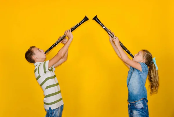 Un niño y una niña tocan el clarinete y se paran uno contra el otro, sobre un fondo amarillo . —  Fotos de Stock