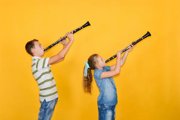 Músicos de niño y niña tocando el clarinete, sobre un fondo amarillo . — Foto de Stock