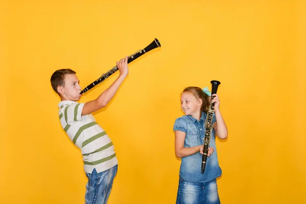 Músicos de niño y niña tocando el clarinete, sobre un fondo amarillo . — Foto de Stock