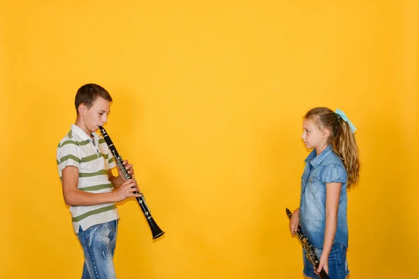 Músicos de niño y niña tocando el clarinete, sobre un fondo amarillo . — Foto de Stock