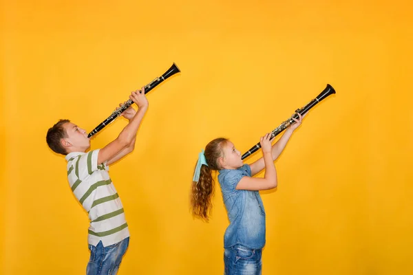 Músicos de niño y niña tocando el clarinete, sobre un fondo amarillo . — Foto de Stock