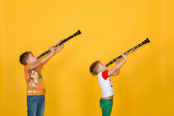 Dos chicos tocan el clarinete y lo sostienen, sobre un fondo amarillo . — Foto de Stock