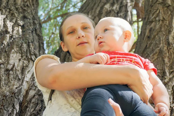 Giovane madre tiene in braccio un bambino piccolo, contro lo schienale — Foto Stock