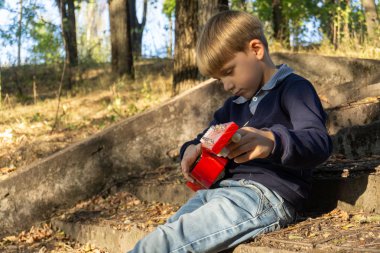 Mavi ceketli ve kot pantolonlu bir çocuk terk edilmiş bir parkta eski basamaklarda gitar çalıyor..