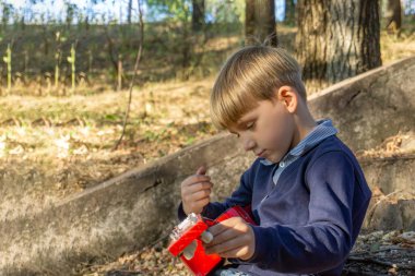Mavi ceketli ve kot pantolonlu bir çocuk terk edilmiş bir parkta eski basamaklarda gitar çalıyor..
