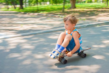 Çocuk asfalt bir yolda kaykayın üstünde oturuyor..