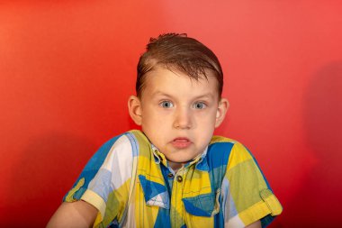 Şaşırmış çocuk omuz silker ve kırmızı bir arka planda ne yapacağını bilmez.