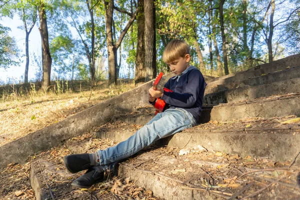 Egy fiú kék kabátban és farmerben gitározik a régi lépcsőkön egy elhagyatott parkban.. — Stock Fotó