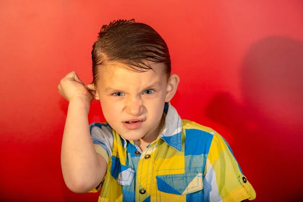 Menino irritado em uma camisa xadrez em um fundo vermelho — Fotografia de Stock