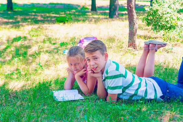 Menino com uma menina fazendo lição de casa na grama no parque . — Fotografia de Stock