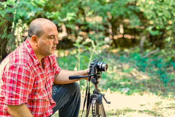 Mężczyzna fotograf kontroluje kamerę na statywie w parku. — Zdjęcie stockowe