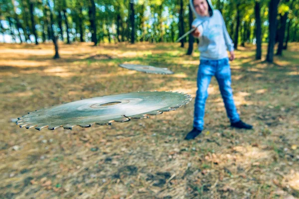 De man gooit een cirkelvormig mes om de vijand in het bos aan te vallen, schijven van een cirkelzaag vliegen in de camera. — Stockfoto