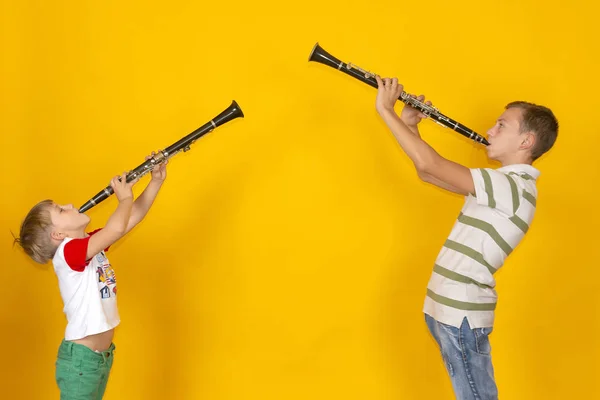 Dois rapazes tocam clarinete e seguram-no, num fundo amarelo. — Fotografia de Stock