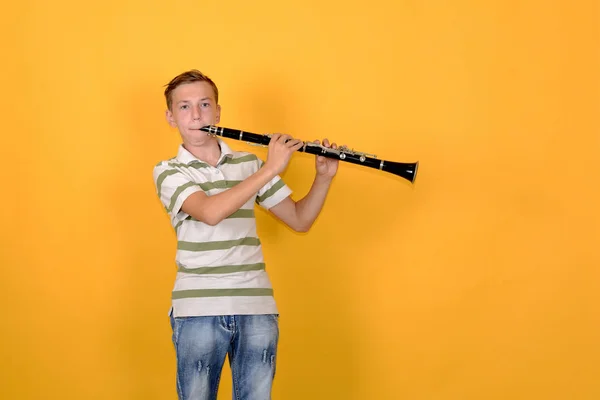 Muzyk chłopiec gra na klarnecie na żółtym tle. — Zdjęcie stockowe