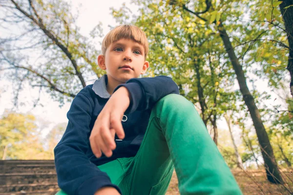 Ein Junge sitzt auf den Stufen in einem alten verlassenen Park, Blick von unten. — Stockfoto