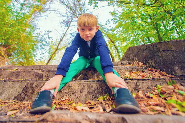 Un niño se sienta en las escaleras en un viejo parque abandonado, vista desde abajo . — Foto de Stock