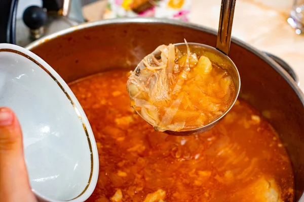 The hostess pours red borsch with cabbage and fatty fat, meat in a soup ladle and an empty plate. — Stock Photo, Image