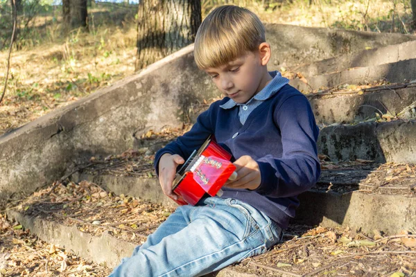 Egy fiú kék kabátban és farmerben gitározik a régi lépcsőkön egy elhagyatott parkban.. — Stock Fotó