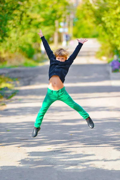 Мальчик в зеленых штанах подпрыгивает от радости в парке на прогулке . — стоковое фото