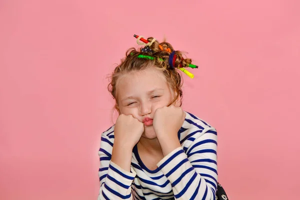 Une fille avec une coiffure drôle dans un T-shirt rayé touche ses cheveux, est surprise et fait des visages drôles . — Photo