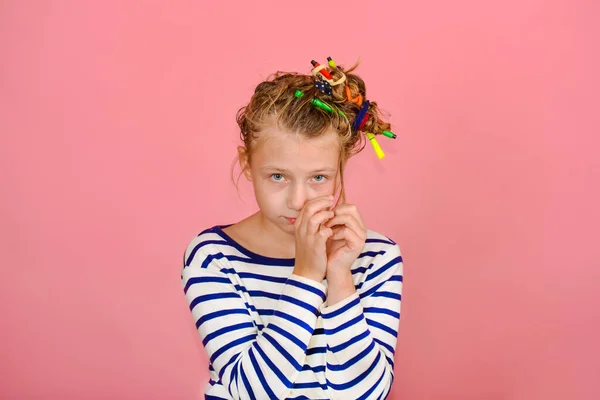 Una chica con un peinado divertido en una camiseta a rayas toca su cabello, se sorprende y hace caras graciosas . —  Fotos de Stock