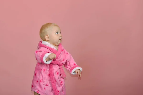Little girl looks away in a pink bathrobe on a pink background in the studio. — Stock Photo, Image