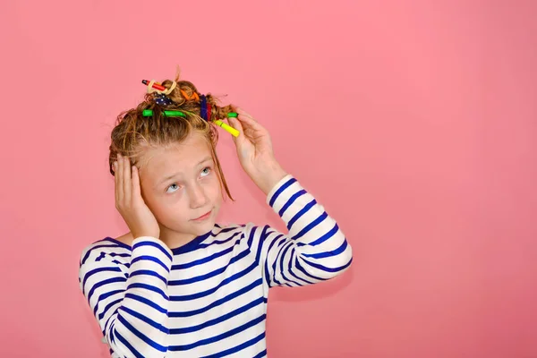 Una chica con un peinado divertido en una camiseta a rayas toca su cabello, se sorprende y hace caras graciosas . —  Fotos de Stock