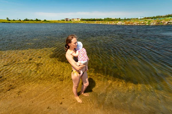 Mama trzyma dziecko w ramionach, stojąc w wodzie na rzece. — Zdjęcie stockowe