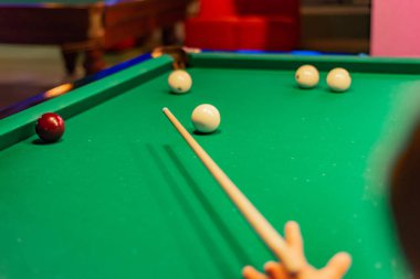 Bir adam elinde bilardo ıstakası ve çekiç toplarını bir cebine koyar..