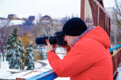Fotograf fotografuje v zimě na kameře v červené bundě a černém klobouku.