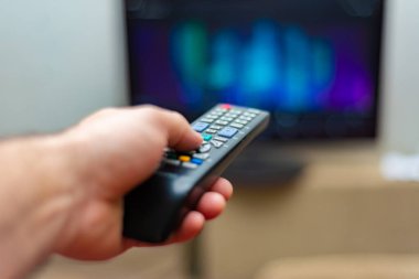 Bir adam televizyon izler ve vites kontrolünü sol eliyle tutar..