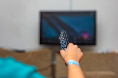 TV kumandalı bir kişi TV izlemek için kanal değiştirmek için uzaktan kumandayı kontrol eder.