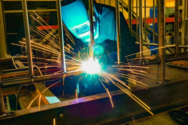 Un soldador trabajando en un taller produce estructuras metálicas. Chispas de soldadura vuelan alrededor . — Foto de Stock