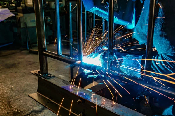 Un saldatore al lavoro in un'officina produce strutture metalliche. Le scintille della saldatura volano in giro . — Foto Stock