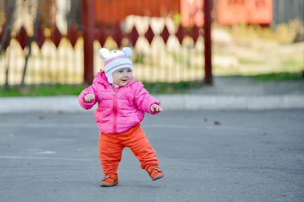 A little girl in a red jacket learns to walk on the road in the fall afternoon. — Stock Photo, Image