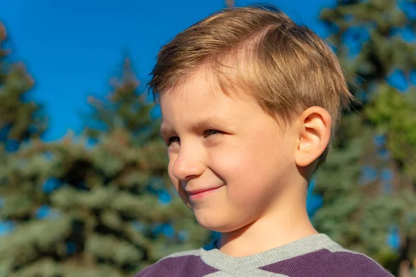 Porträt eines Jungen auf der Straße, der vor blauem Himmel und grünen Weihnachtsbäumen zur Seite schaut. — Stockfoto