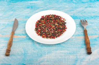 Beyaz bir tabakta baharatlar, bıçak ve çatal mavi ahşap arka planda yakınlarda yatıyor.