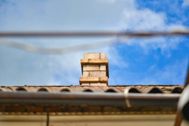Mavi bulutlu gökyüzüne karşı bir apartmanın tahta çatısındaki tuğla baca borusu.