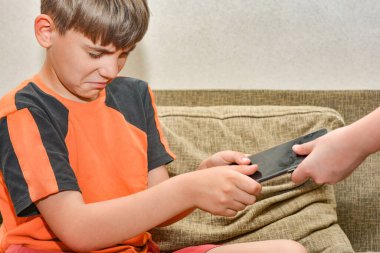 Çocuk ağlıyor, çünkü annesi telefonu elinden alıyor. Sorunlu bir ailede yaramaz ve yaramaz çocuklar