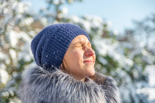 A girl in blue clothes in the winter in a snowy pine forest enjoys the frosty nature. Winter Christmas mood.