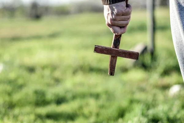 A man holds a wooden Christian cross in front of him, an ax in his other hand. The concept of casting out demons on Halloween.