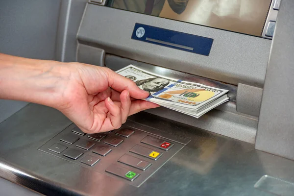 The girl withdraws cash from the ATM. dollars in the hand of a man at the terminal